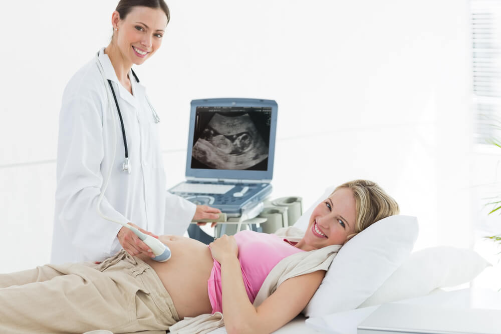 Portrait of Smiling Doctor Using Ultrasound Machine on Pregnant Woman in Clinic