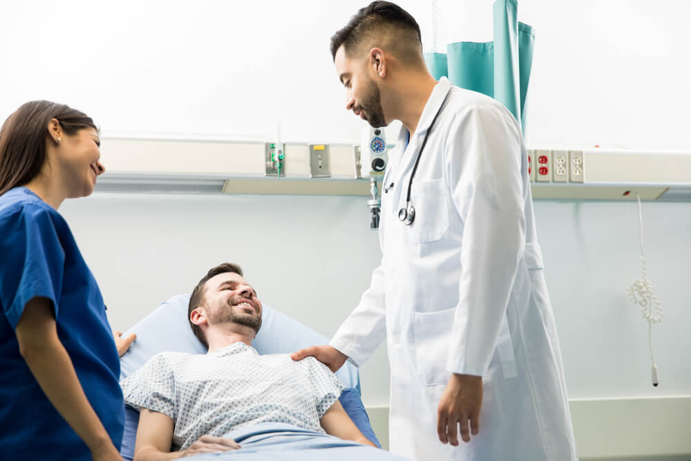 Portrait of a Male Patient on a Hospital Bed Smiling to His Doctors While Recovering From Surgery