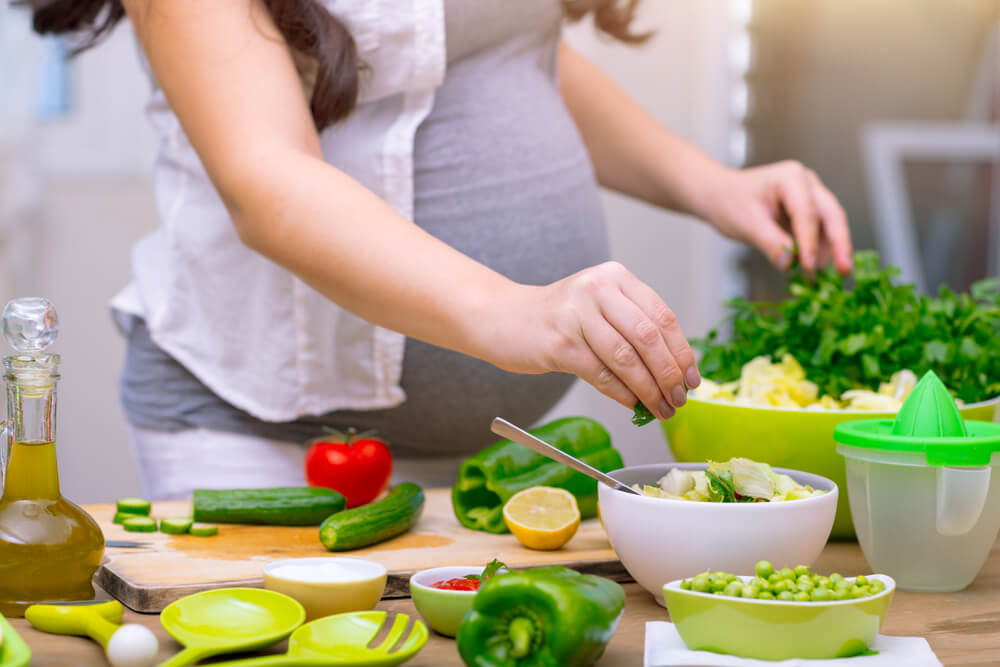 Happy Pregnant Woman Cooking at Home, Doing Fresh Green Salad, Eating Many Different Vegetables During Pregnancy