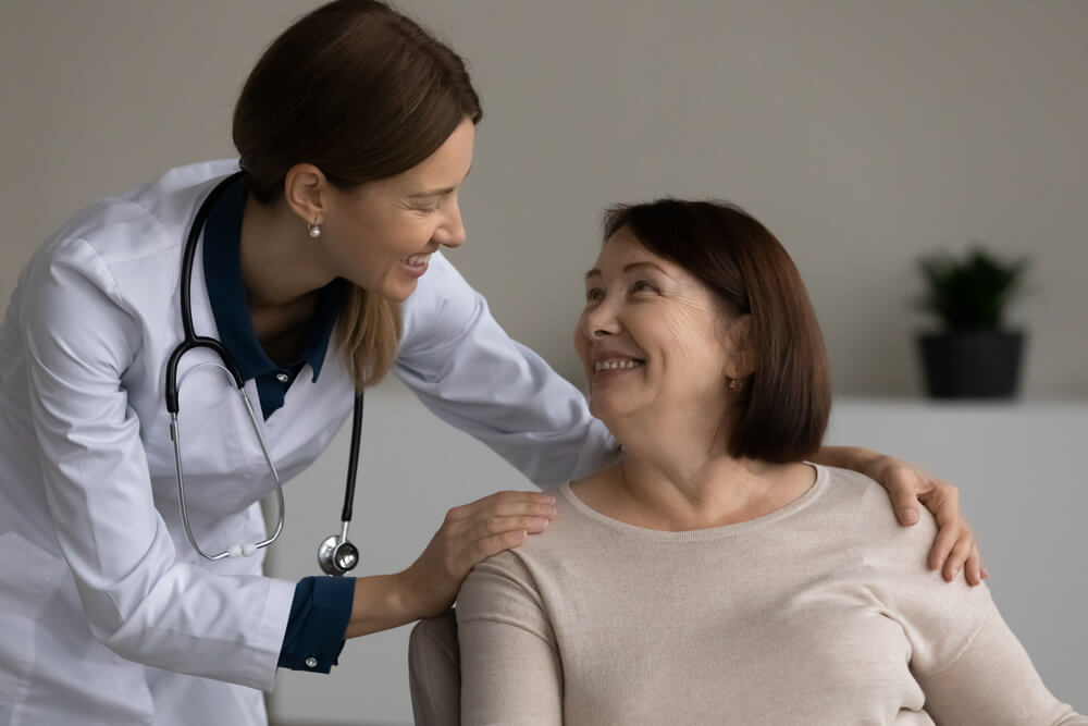 Happy Positive Medical Professional, Doctor, Nurse Giving Support and Help to Senior Female Patient at Appointment, Touching Shoulders.