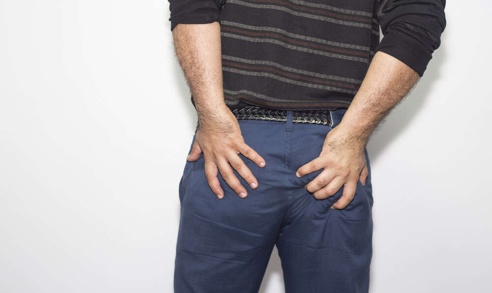 Man With Hemorrhoids Holding His Butt in Pain, in a White Background
