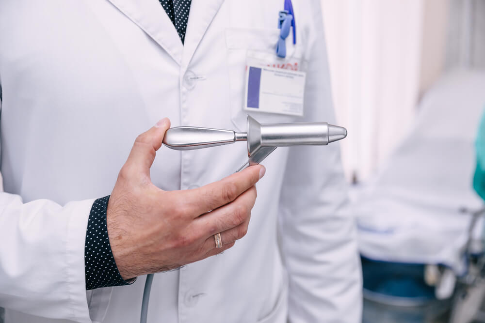 The Doctor’s Hand Holds the Instrument for the Treatment of Hemorrhoids Against the Background of Blurred Medical Instruments in the Operating Room
