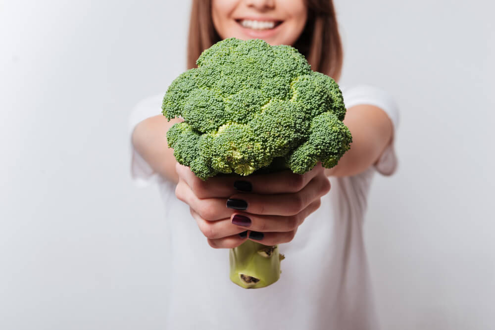 Cropped Image of Young Woman Dressed in White T-Shirt Showing Broccoli to Camera.