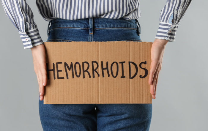 Woman Holding Carton Sign With Word Hemorrhoids on Light Grey Background
