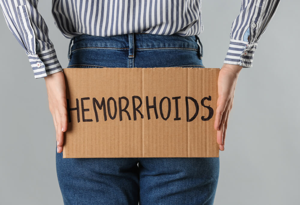 Woman Holding Carton Sign With Word Hemorrhoids on Light Grey Background