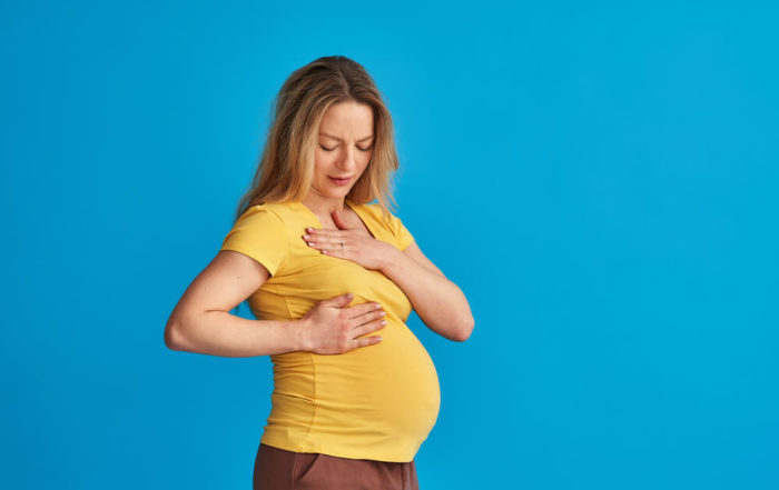 A Frustrated Pregnant Woman Checks Her Breasts for a Seal While Standing on a Blue Studio Background.