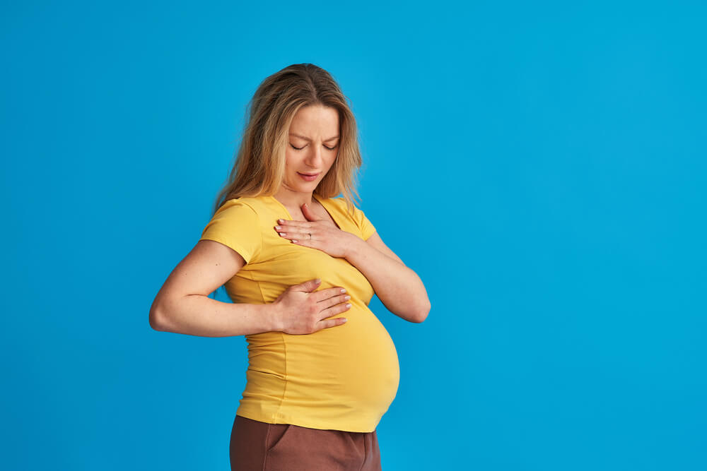 A Frustrated Pregnant Woman Checks Her Breasts for a Seal While Standing on a Blue Studio Background.