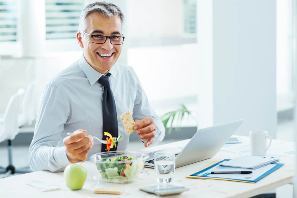 Smiling Businessman Sitting at Office Desk and Having a Lunch Break