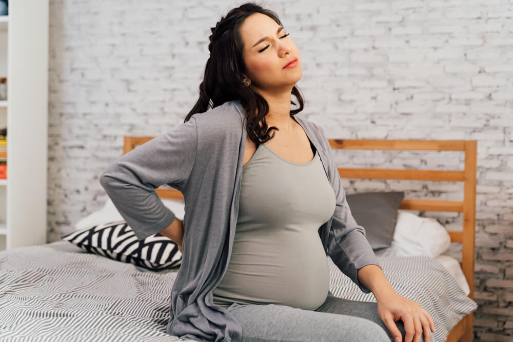 Pregnant Woman Suffering Back Pain Sits on Bed at Home.
