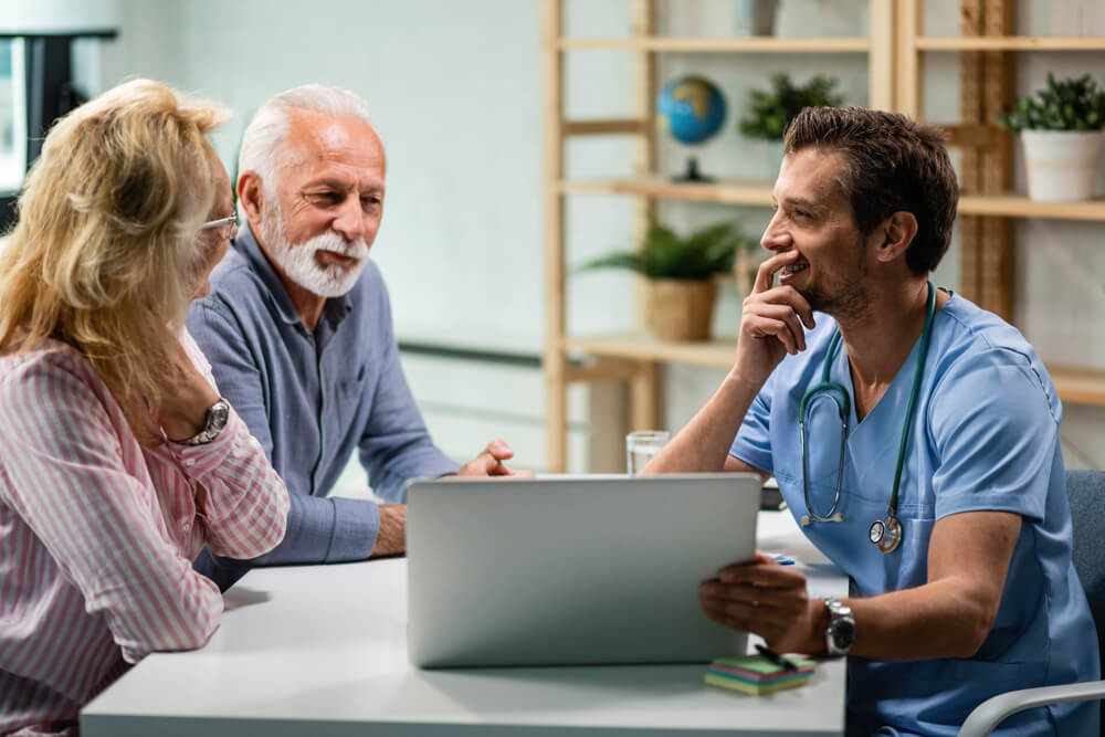 Happy Mature Couple Communicating With Their Doctor While Using Laptop Together. Focus Is on Doctor.