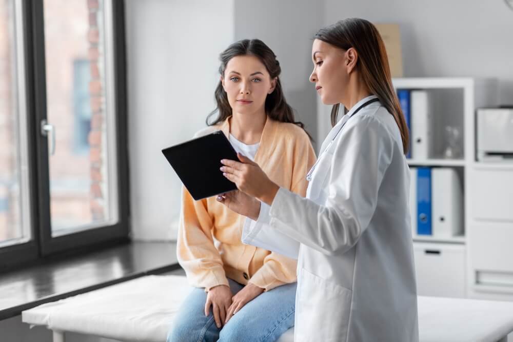 Female doctor with tablet pc computer talking to woman patient at hospital