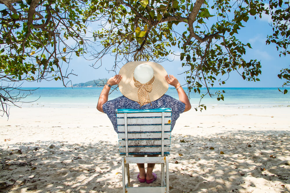 Woman Sitting on a Beach Chair Under a Tree Enjoying a Summer Day at the Beach