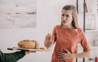Man Holding Cutting Board With Bread Near Upset Blonde Woman With Gluten Allergy