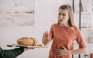 Man Holding Cutting Board With Bread Near Upset Blonde Woman With Gluten Allergy