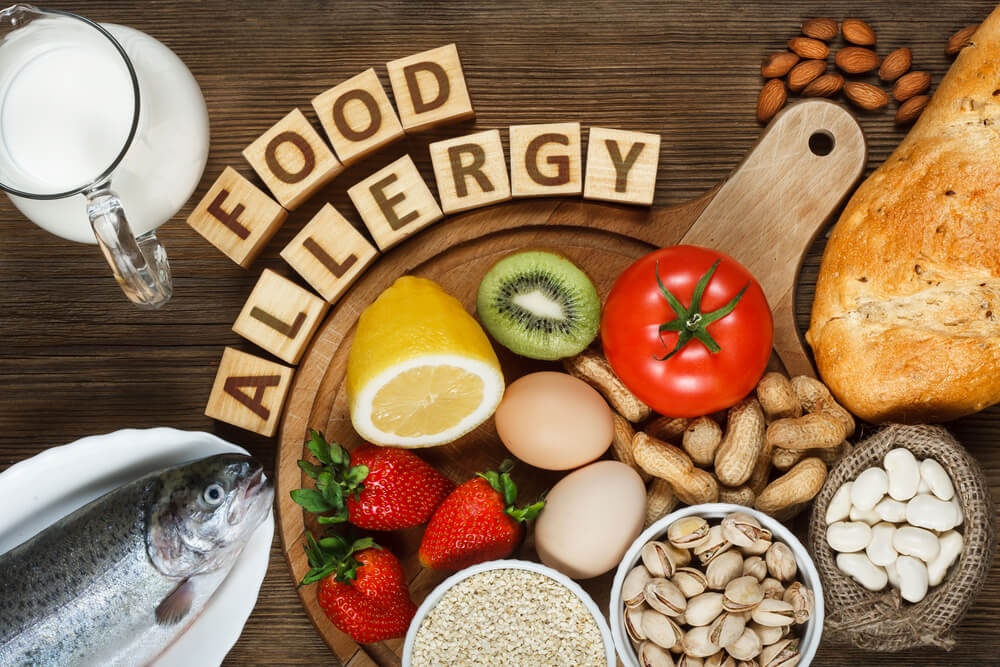 Allergy Food as Almonds, Milk, Pistachios, Tomato, Lemon, Kiwi, Trout, Strawberry, Bread, Sesame Seeds, Eggs, Peanuts and Bean on Wooden Table