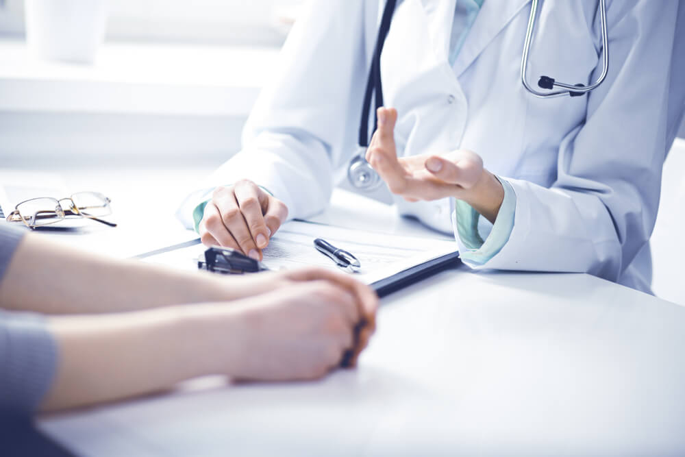 Doctor and Female Patient Sitting at the Desk and Talking in Clinic Near Window