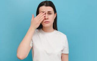 Young Girl Suffering From Eyes Pain and Feeling Something in Eye, Posing on Blue Wall.