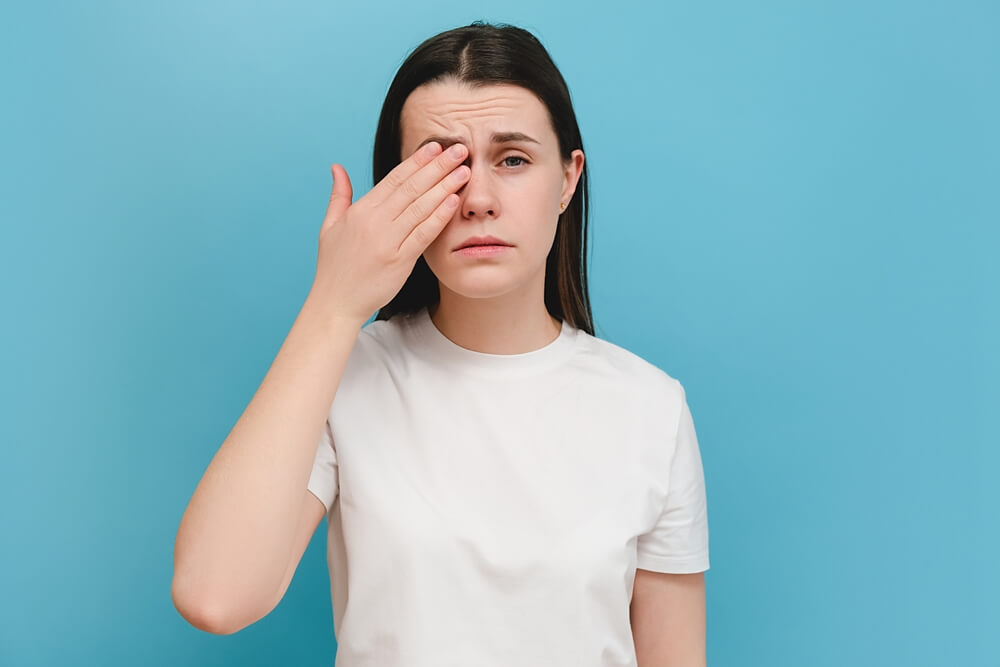 Young Girl Suffering From Eyes Pain and Feeling Something in Eye, Posing on Blue Wall.
