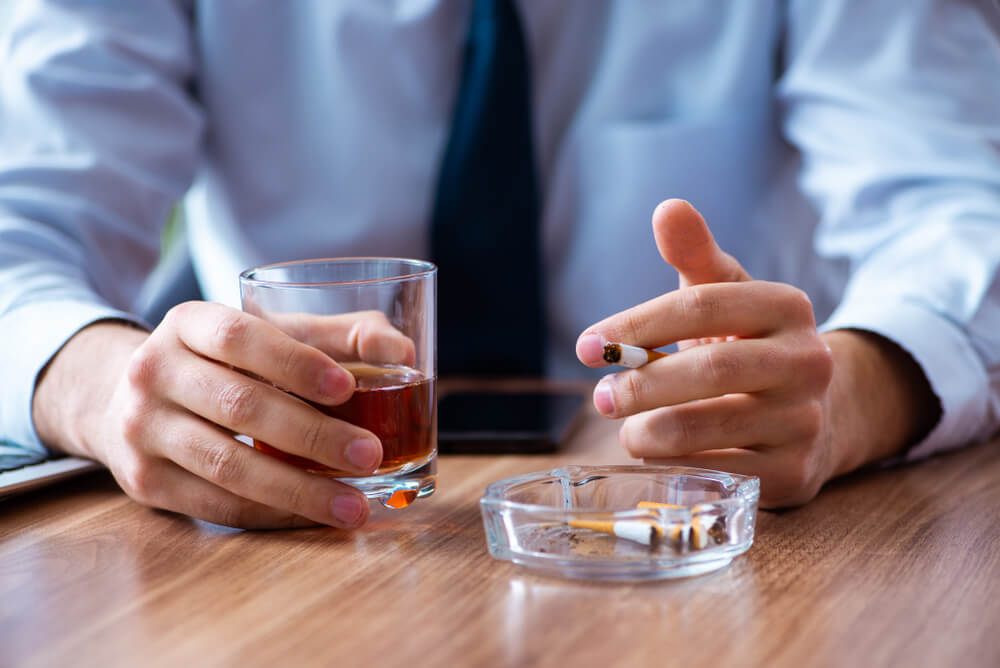 Male Employee Drinking Alcohol and Smoking Cigarettes at Workplace