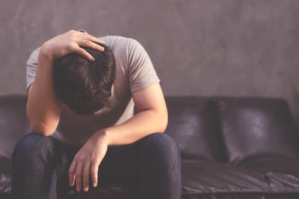 Depressed Man Sitting on the Sofa and Holding His Forehead