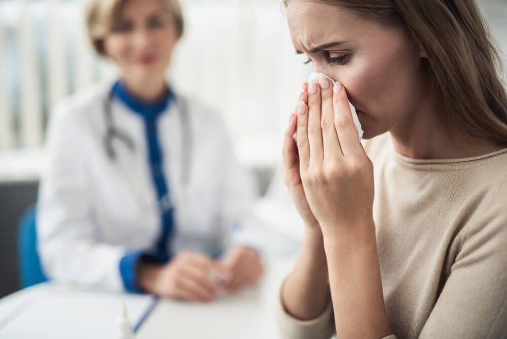 Close Up Portrait of Young Female Patient Blowing Nose While Consulting in Medical Office