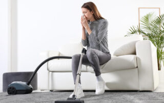 Young woman suffering from dust allergy while vacuuming house