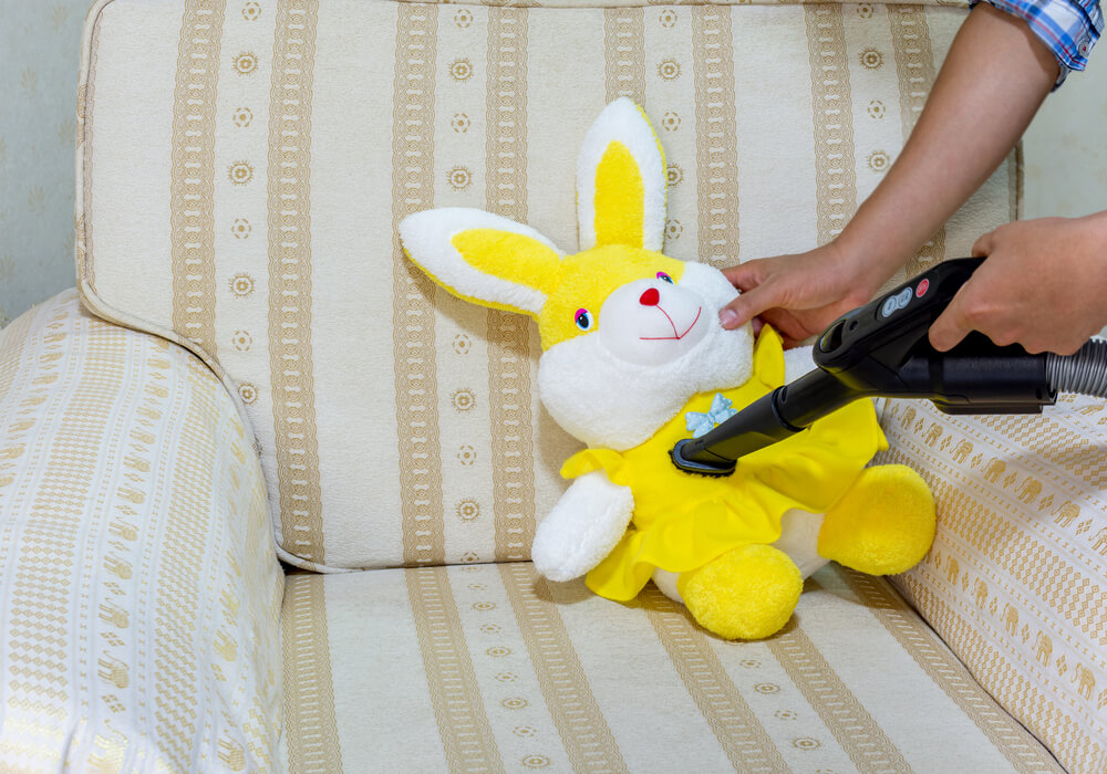 A person is using a vacuum cleaner to clean the doll to prevent dust and dust mites that cause allergies.