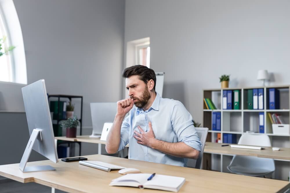 Sick man working in the office, has a bad cough, coughing businessman at the computer