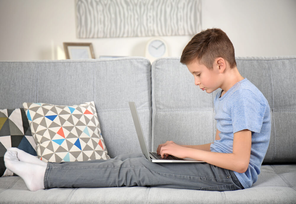 Schoolboy With Laptop Sitting on Sofa