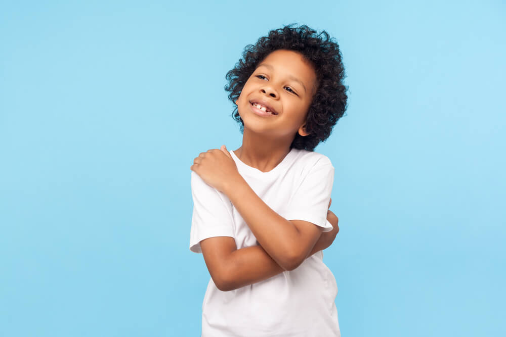  Portrait of Adorable Optimistic Little Boy With Curls Embracing Himself and Smiling