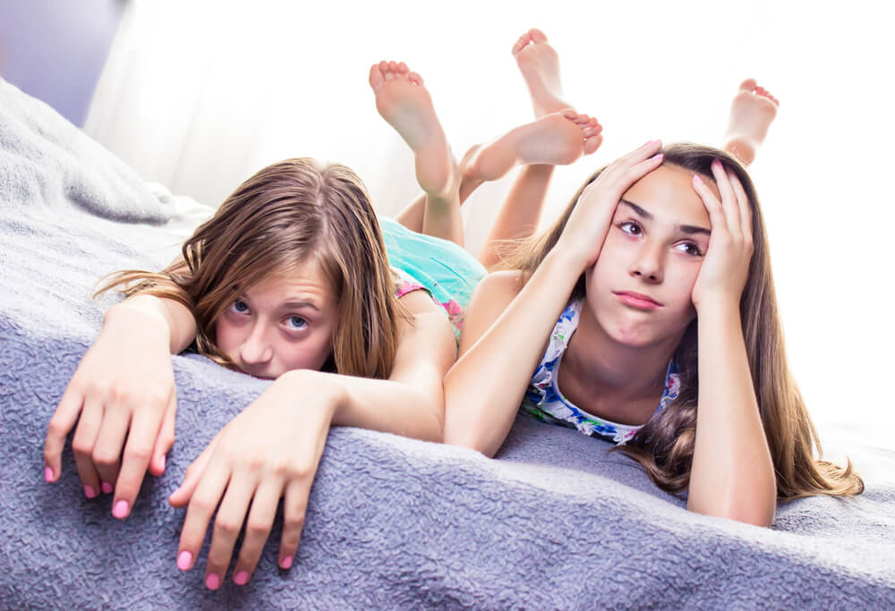 Two Cute, Teenage Girls Lying on the Bed, Looking Very Bored.