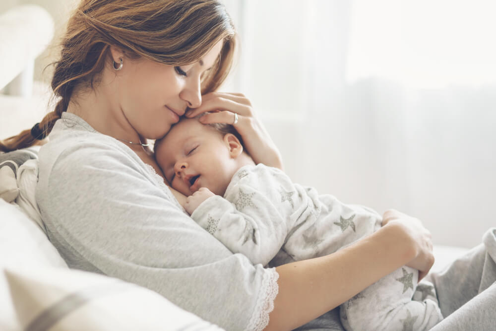 Bright Portrait of Happy Mum Holding Sleeping Infant Child on Hands.