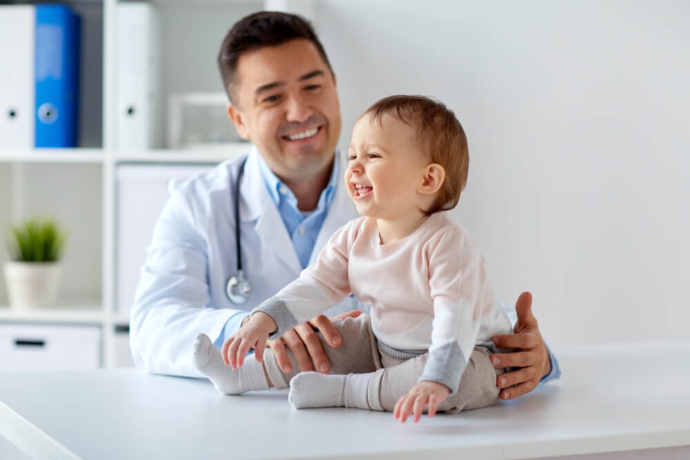 Medicine, Healtcare, Pediatry and People Concept - Happy Doctor or Pediatrician Holding Baby on Medical Exam at Clinic