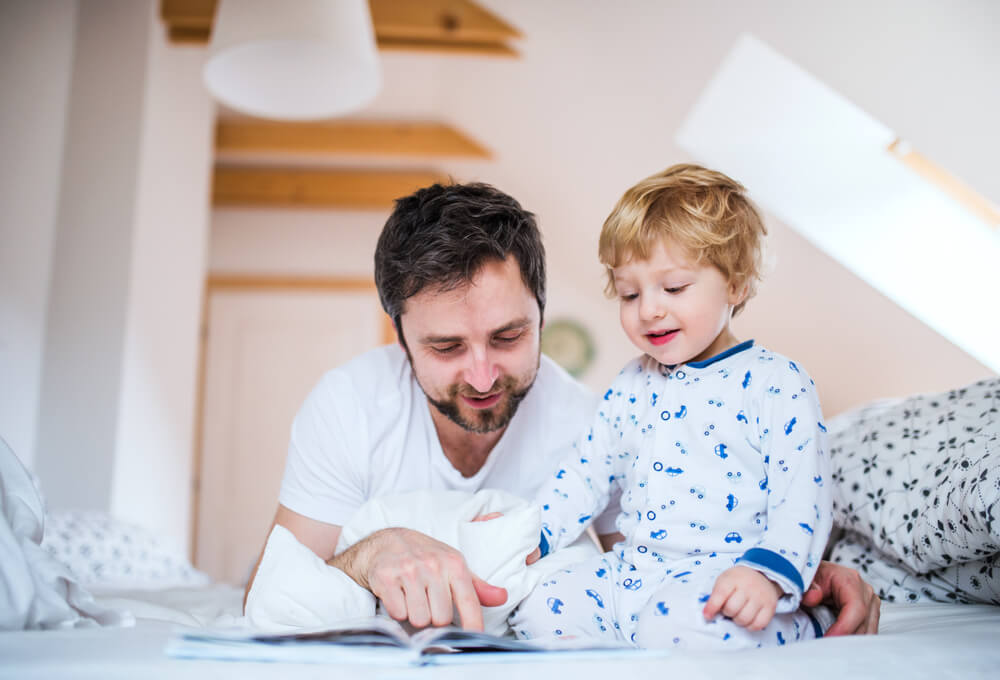 Father With Toddler Boy Reading a Book on Bed at Home at Bedtime