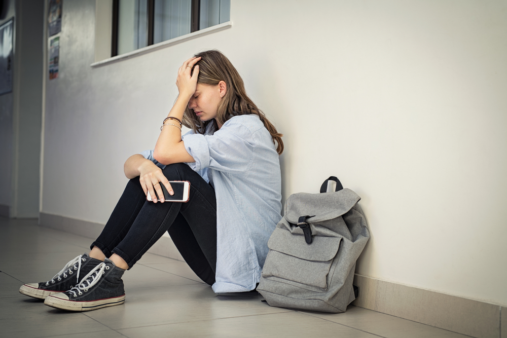 Upset And Depressed Girl Holding Smartphone Sitting On College Campus