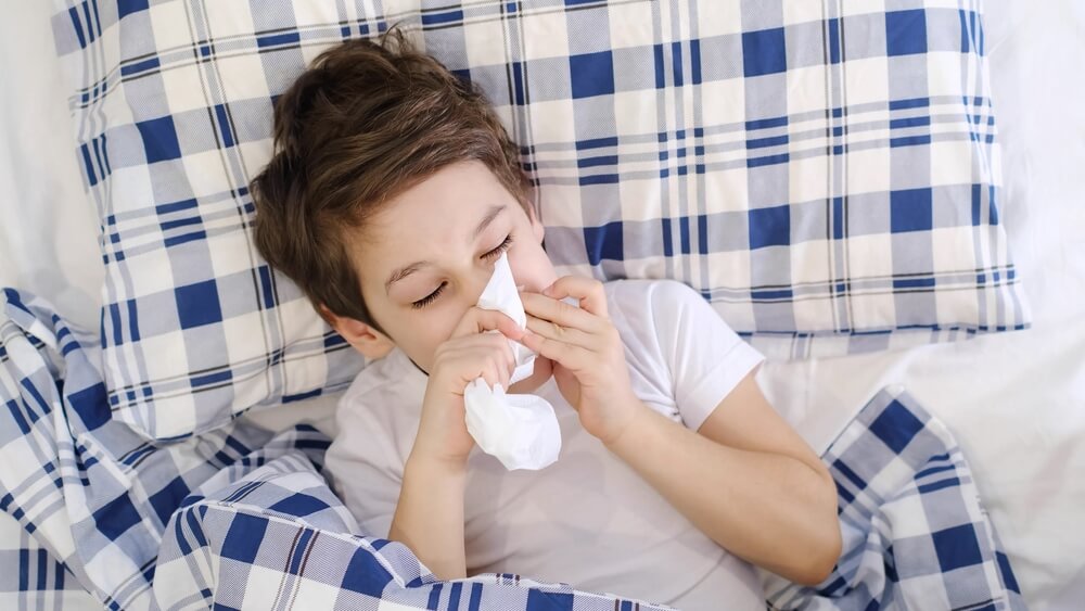 Child cold flu illness tissue blowing runny nose. toddler boy is lying in bed and blowing nose into tissue paper at home. Allergy