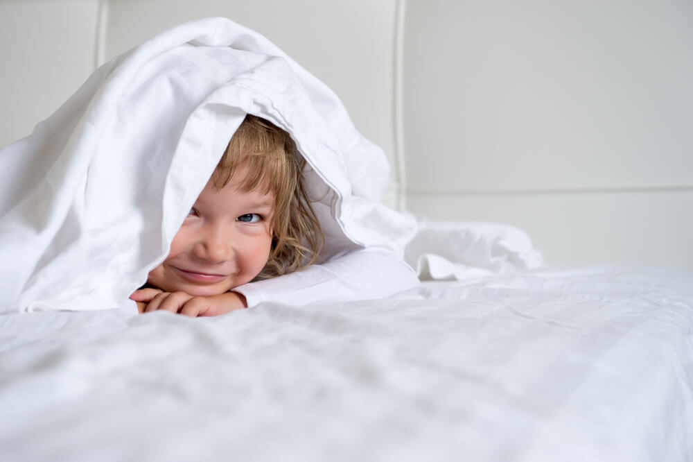 Morning Awakening in Nightwear. Cute Little Girl Dabbles in White Bed