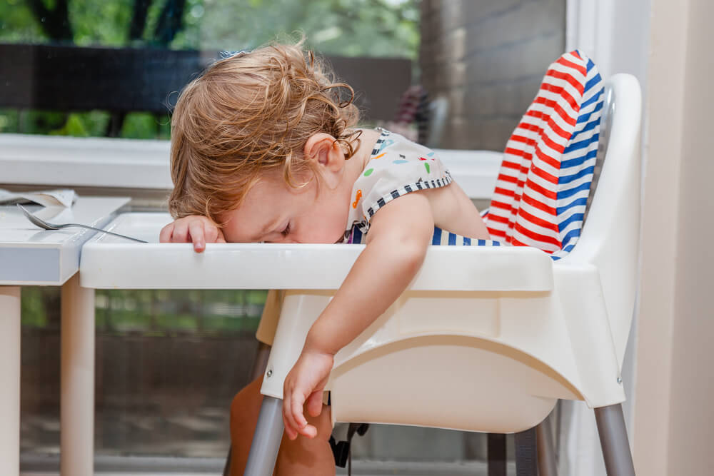 Tired Child Sleeping In Highchair After The Lunch. Baby Over Eating And Fall Asleep Just After Feeding, Lying His Face On The Table Tray.