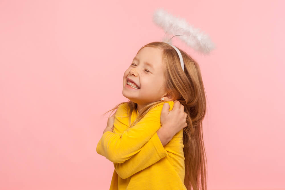 I Love Myself. Beautiful Charming Little Girl With Halo Over Head Embracing Herself And Smiling From Happiness,