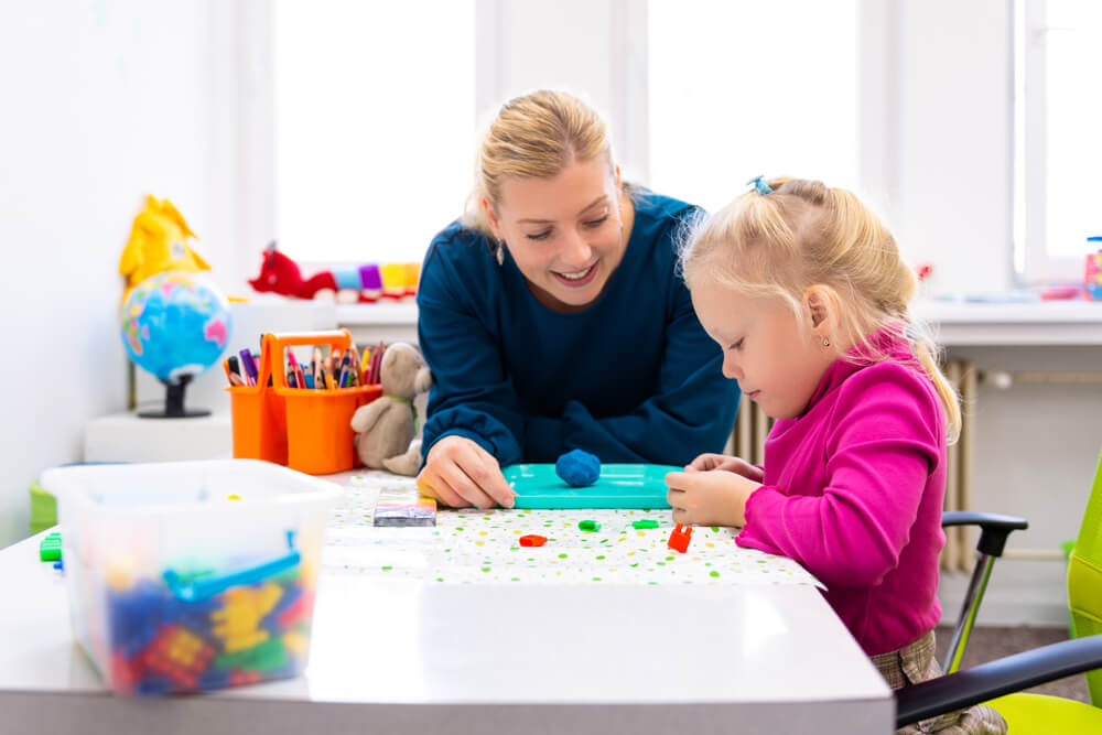 Toddler girl in child occupational therapy session doing sensory playful exercises with her therapist.