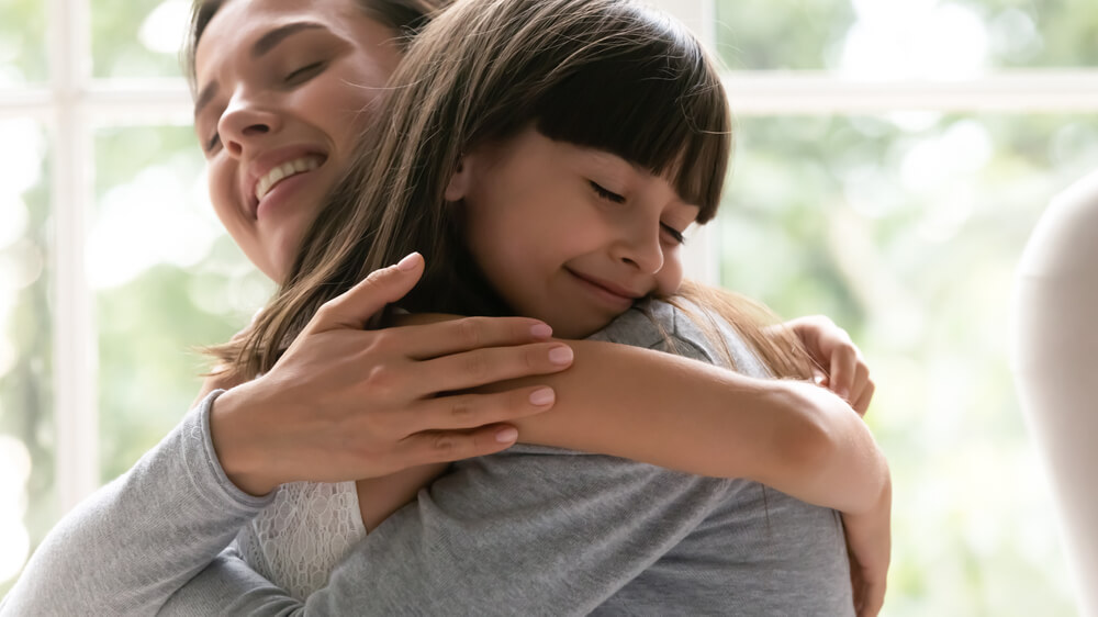A young girl embraces her mother tightly, seeking comfort and support in the face of cyberbullying, highlighting the crucial role of parental guidance and emotional support in addressing this issue.
