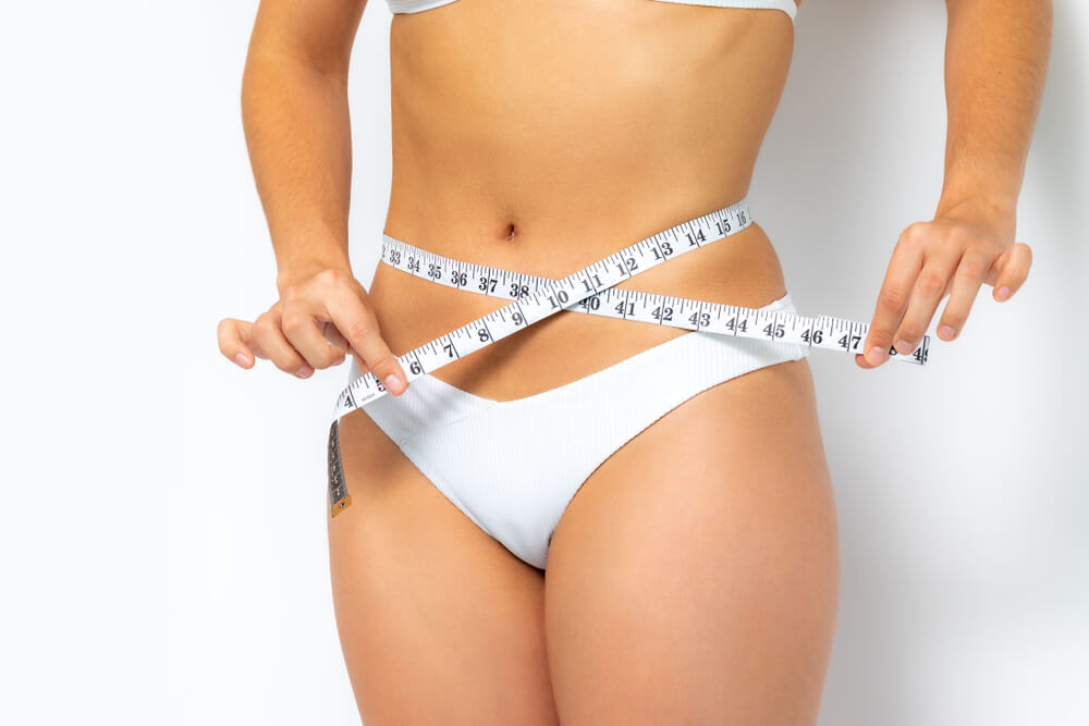 Close up Female Waist in White Bikini. Hands Measuring Waist With Metric Band.