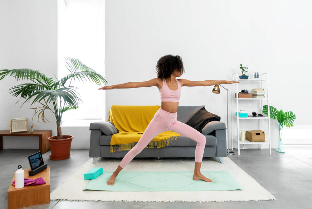 Afro Woman Practicing Warrior II Pose Using Online Yoga Training Program in the Tablet at Home