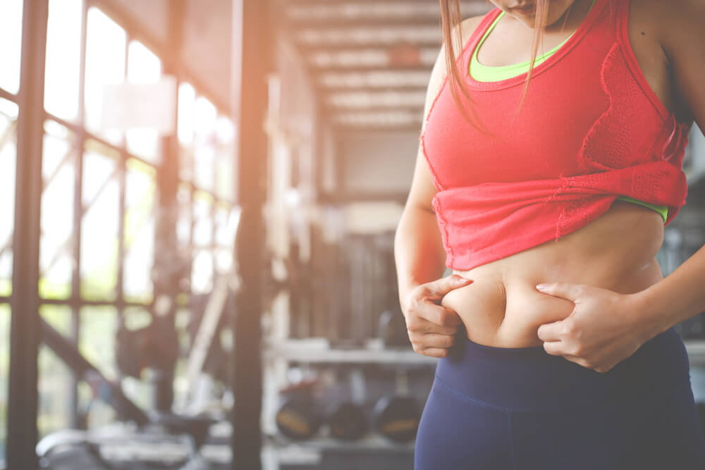 Obese Woman Hand Holding Excessive Belly Fat Isolated on Gym Background