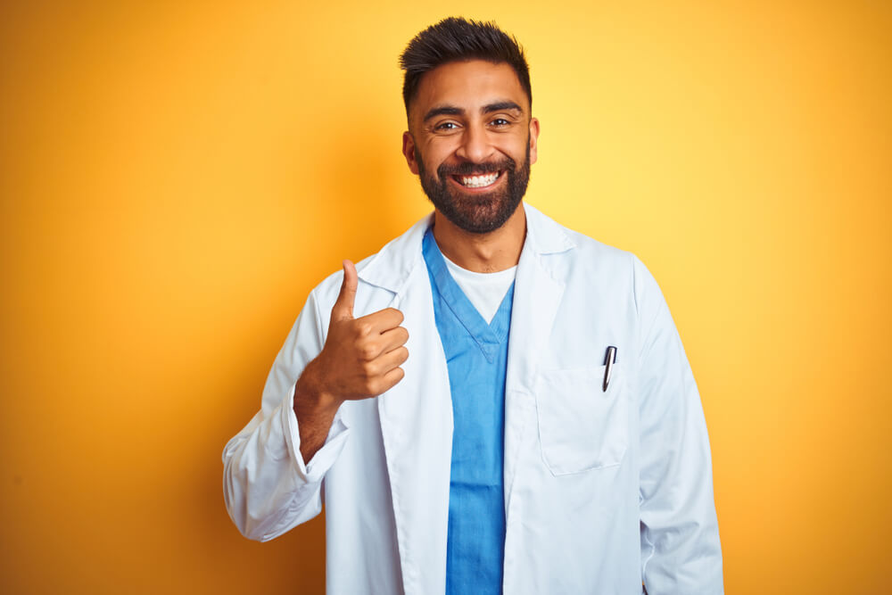 Young Indian Doctor Man Standing Over Isolated Yellow Background Doing Happy Thumbs up Gesture With Hand.