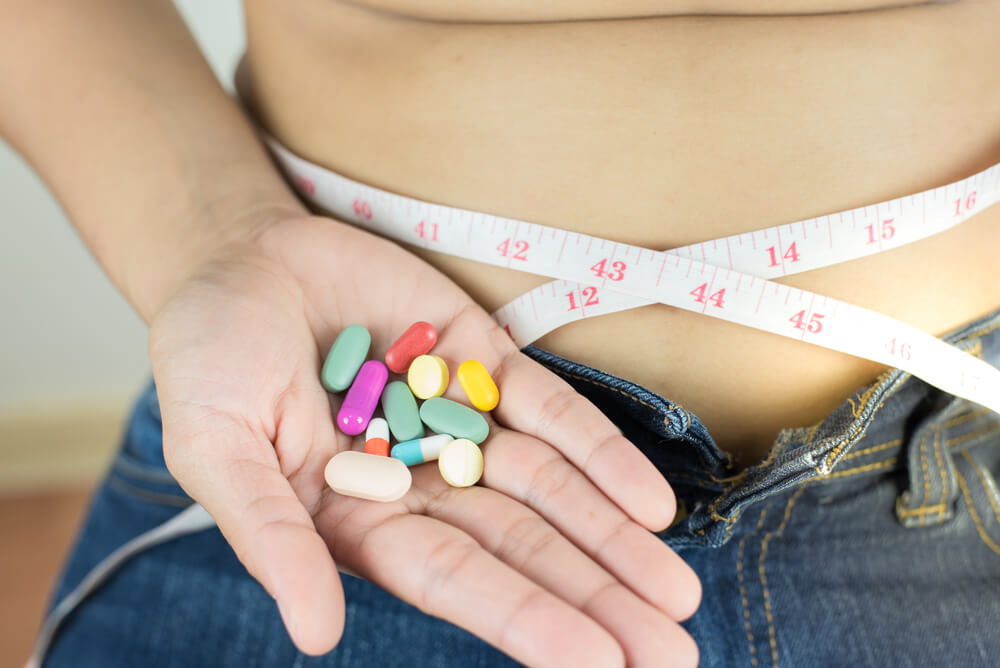 Weight Loss Unhealthy and Dangerous Concept, Woman Measuring Her Waist With Many Slim Pills in Her Hand