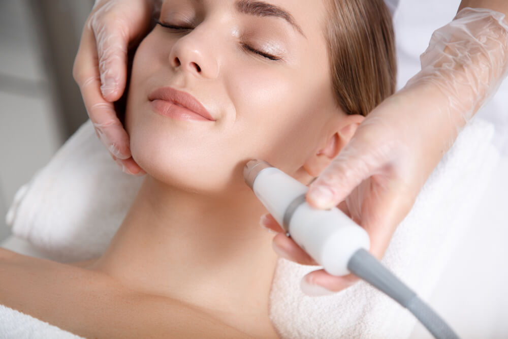 Close Up of Beautician Hand Making Ultrasound Facial Procedure by Special Equipment.