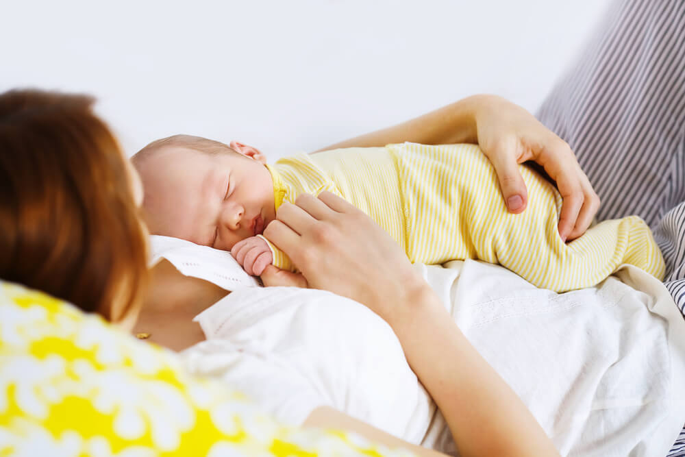 Newborn Sleeping Child in the Hands of Mother. Young Beautiful Mother Recovering After Childbirth.