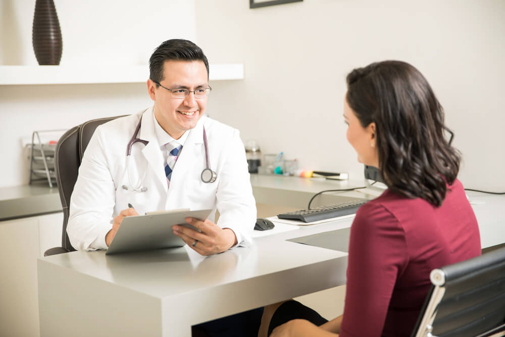 Hispanic Doctor Taking Some Notes and Talking to a Patient During a Consultation at His Office