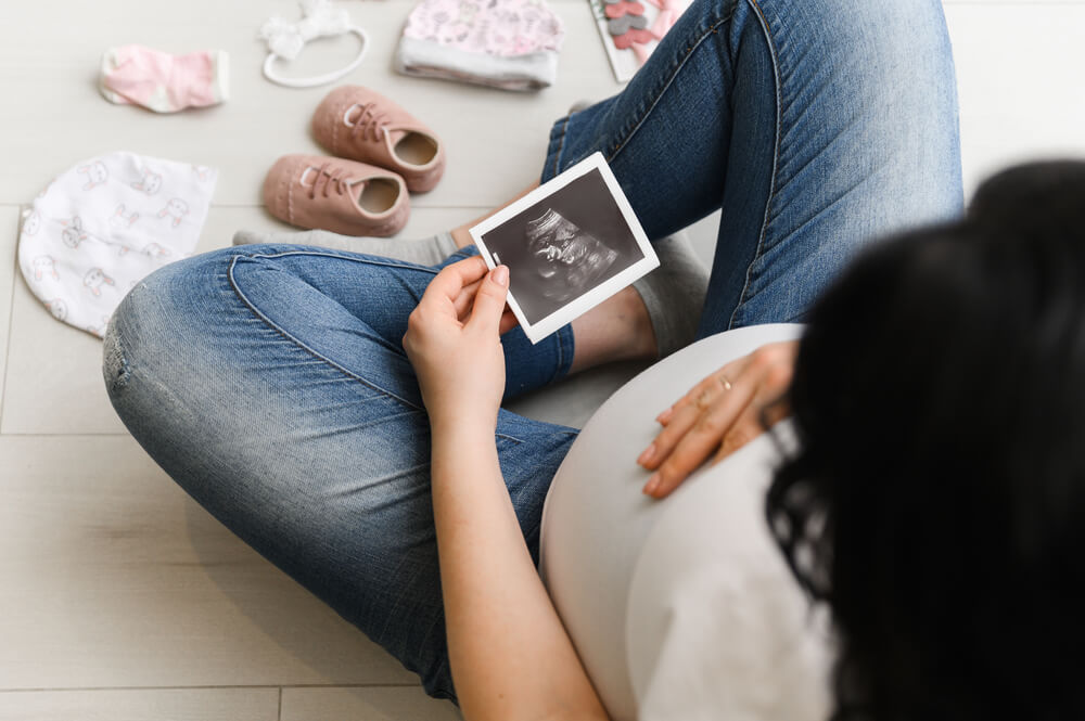 Pregnant Woman Enjoying Future Motherhood With Her Baby’s First Ultrasound Photo, Top View With Free Space